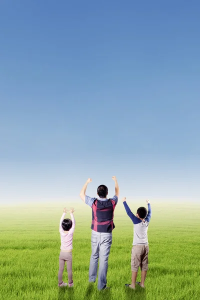 Los niños y su padre levantan las manos en el campo Fotos de stock libres de derechos