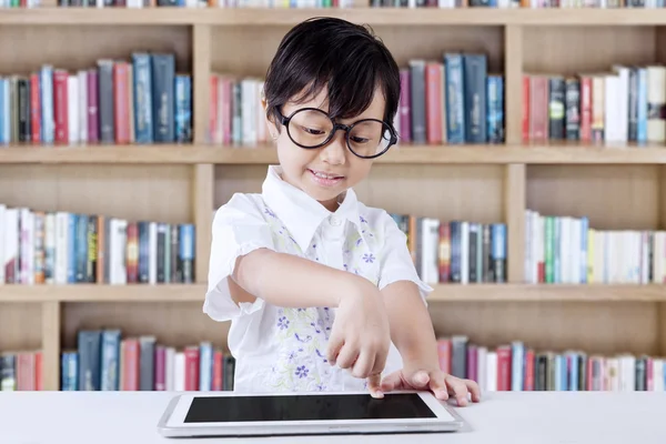 Malá holčička používá tabletu v knihovně — Stock fotografie