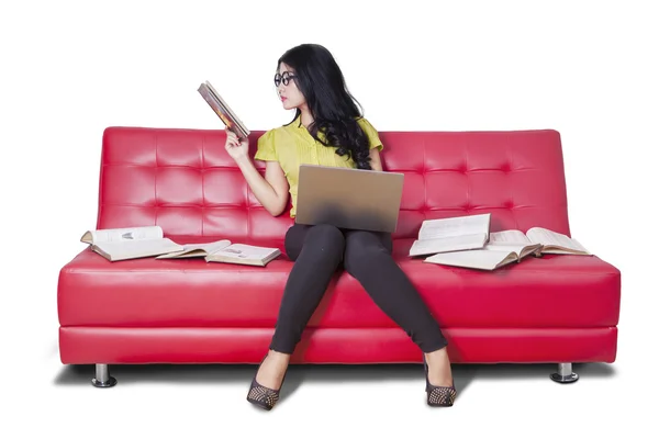 Студент читает книги и пользуется ноутбуком на диване — стоковое фото