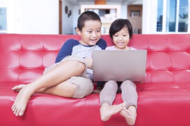 İki oğul evde kanepede dizüstü bilgisayar kullanarak