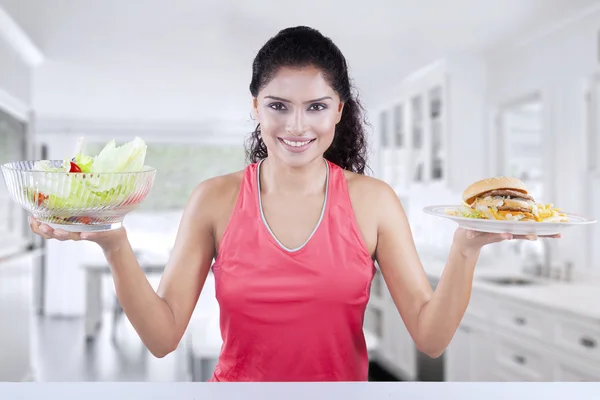 Woman comparing salad and hamburger — Stock Photo, Image