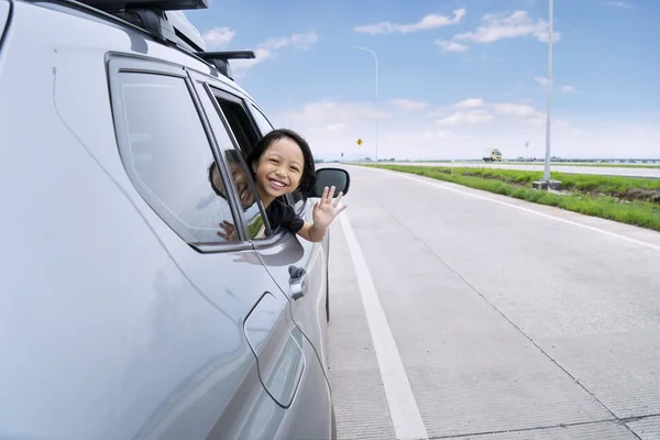 Cheerful little girl waving hand in the car — Stock Photo, Image
