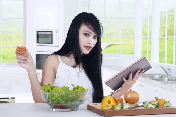 Woman reads book and prepare salad — Stock Photo, Image