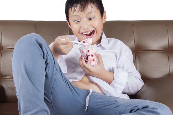 Cheerful boy eats ice cream on sofa — Stock Photo, Image