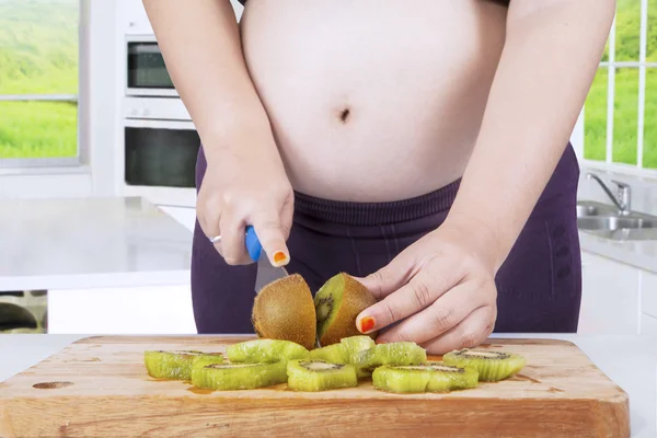 Zwangere vrouw kiwi fruit snijden — Stockfoto