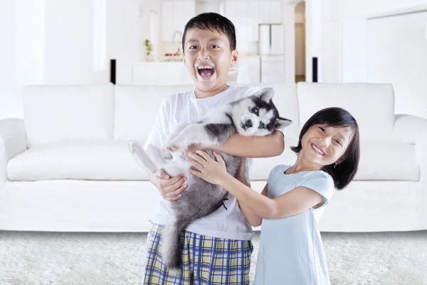 Feliz niños sosteniendo husky cachorro en casa — Foto de Stock