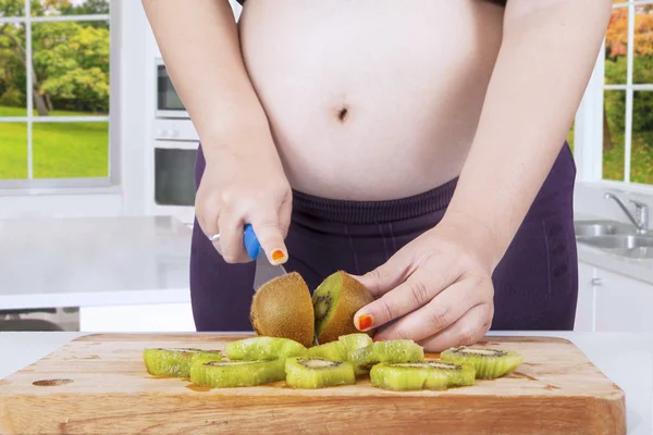 Mãe grávida cortando kiwi frutas na cozinha — Fotografia de Stock