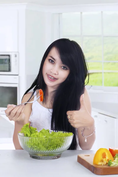 Mulher com sinal OK come salada na cozinha — Fotografia de Stock