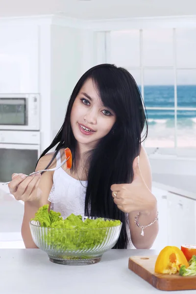 Jovem mulher gosta de salada na cozinha — Fotografia de Stock