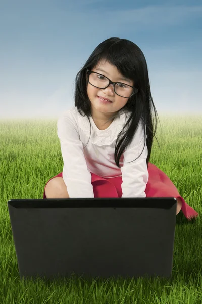 Adorable girl sits on the grass with laptop — Stock Photo, Image