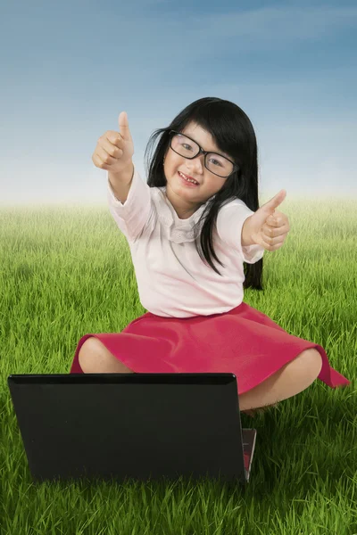 Ребенок показывает знак ОК с ноутбуком на траве — стоковое фото