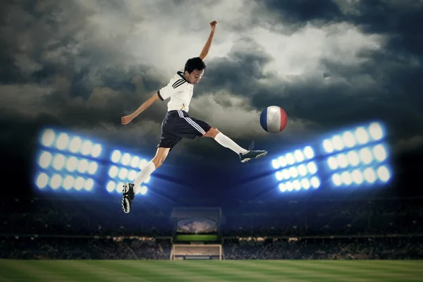 Football player jumping while kicking a ball — Stock Photo, Image