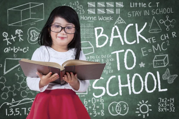 Маленька дівчинка з книгою та каракулями на дошці — стокове фото