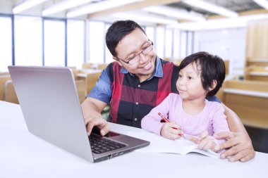 Öğretmen kız öğrencinin çalışmaya yardımcı olur.