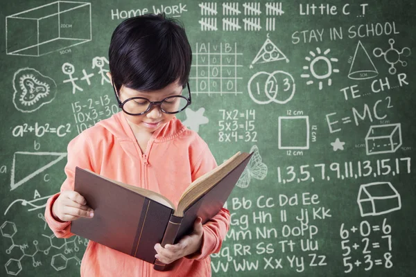 Meisje leest boek met doodles op schoolbord — Stockfoto