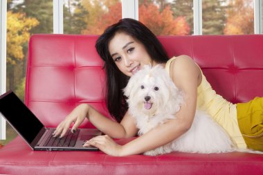 Kadın köpeği ile kanepede dizüstü bilgisayar kullanır