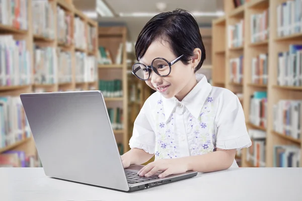 Liten flicka med bärbar dator i biblioteket — Stockfoto