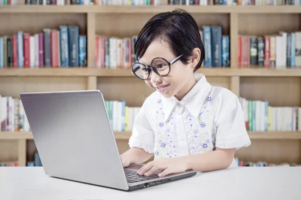 Pequena estudante usa laptop na biblioteca — Fotografia de Stock