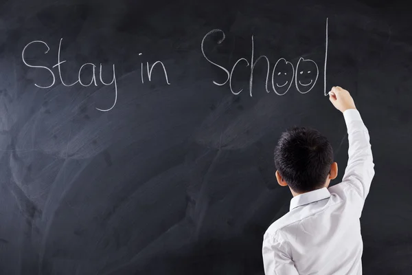 Маленький хлопчик пише текст "Залишайся в школі" — стокове фото
