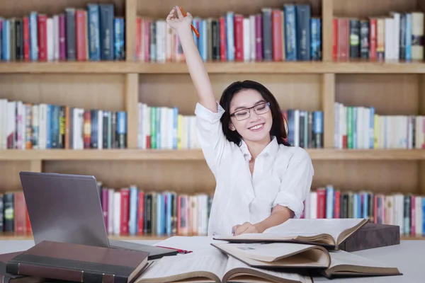 Allegro studentessa alzando la mano in biblioteca — Foto Stock