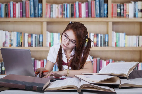 Schoolgirl studying in library with notebook Stock Picture
