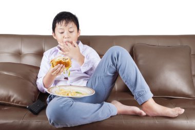 Çocuk kanepede hamburger yiyor