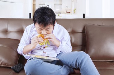 Evde kanepeye hamburger ısıran çocuk