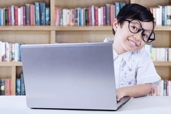 Criança senta-se na biblioteca com laptop — Fotografia de Stock