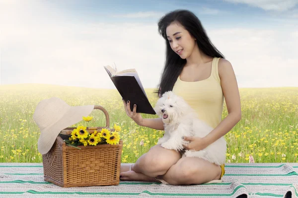 Kvinna och hund läsa bok på äng — Stockfoto