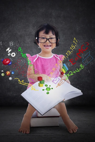 Nettes kleines Mädchen liest Buch mit Formel — Stockfoto