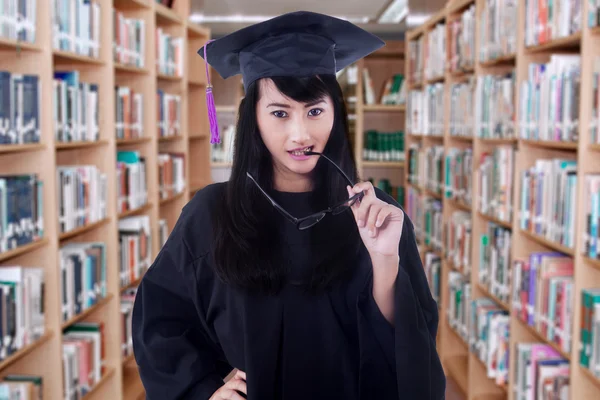 Female bachelor bites an eyeglasses in library — Stock Photo, Image