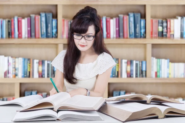 Estudante feminina escrevendo na biblioteca — Fotografia de Stock