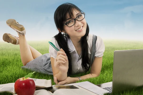 Pretty Asian schoolgirl studying at field — Stock Photo, Image