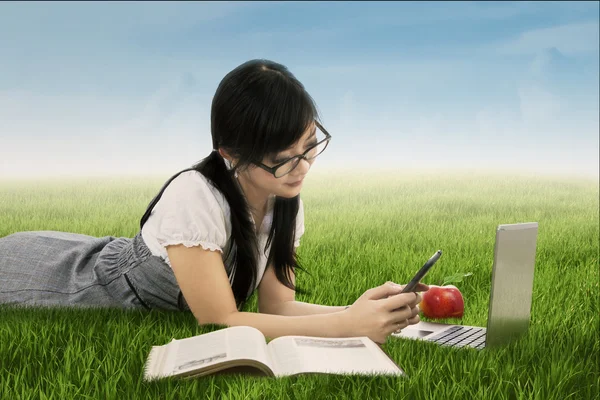 Student texting on her smartphone at field — Stock Photo, Image