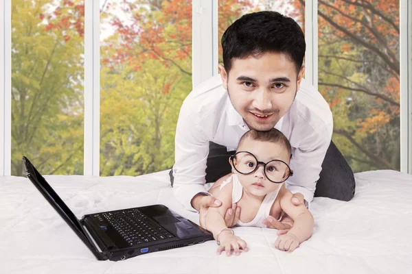 Pappa med söt baby och laptop på säng — Stockfoto