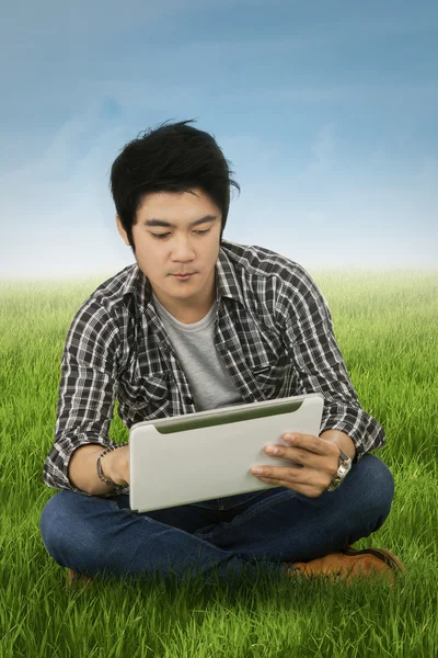 Handsome student uses tablet at field — Stock Photo, Image