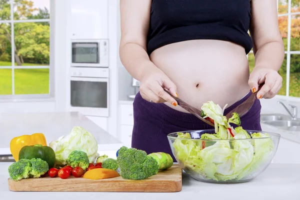 Pregnant woman cooks salad in kitchen — Stock Photo, Image