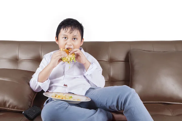 Chico disfrutar de hamburguesa con queso mientras mira la televisión —  Fotos de Stock
