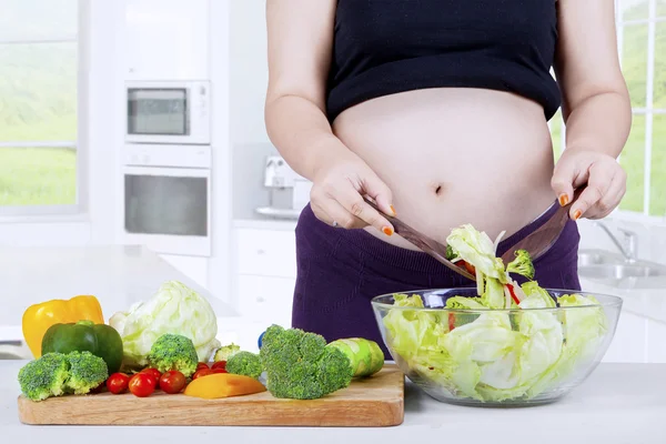 Mujer embarazada prepara ensalada con un tazón —  Fotos de Stock