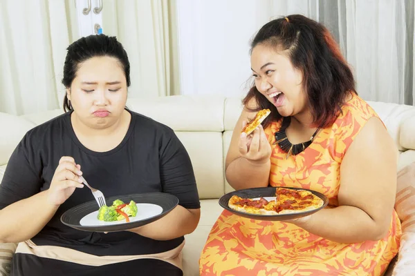 减肥的概念 不快乐的胖女人一边吃沙拉 一边被姐姐嘲笑地吃披萨 — 图库照片