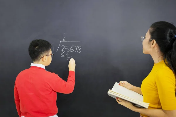 男性学生の写真は 黒板に書いて教室に立っている間に 彼の女性教師と数学を学びます — ストック写真