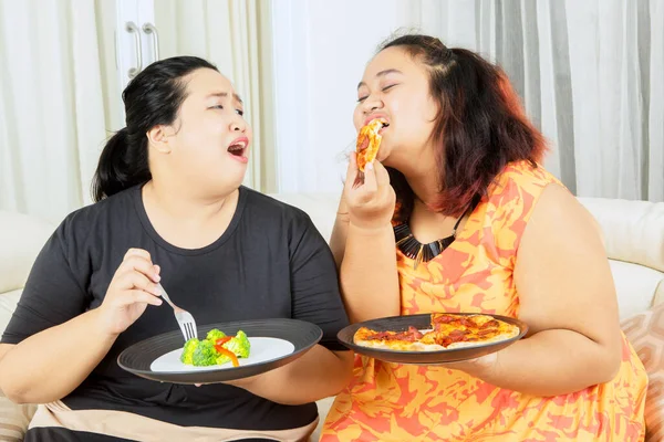 체중을 줄이는 비만증 여성이 거실에서 여동생과 샐러드를 먹으면서 피자를 있습니다 — 스톡 사진