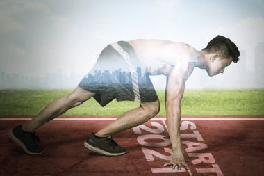 Başlangıç çizgisi üzerinde diz çökmüş genç bir adam ve 2021 numara modern şehir arka planıyla koşmaya hazır.