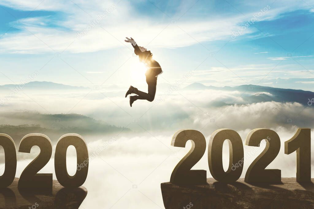 Caucasian businessman jumping through gap from number 2020 to number 2021 with misty mountain background. Shot at sunrise time