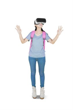 Stüdyoda beyaz arka planda izole bir şekilde dururken sanal gerçeklik gözlüğü kullanan bir lise öğrencisi.