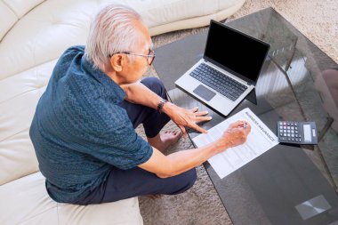 Üst düzey bir adam laptop ve hesap makinesinin yanında sigorta formunu dolduruyor. Evde vuruldu.