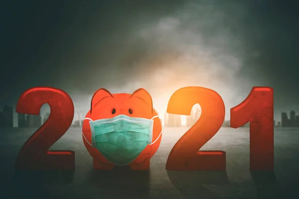 Close up of piggy bank wearing face mask with number 2021 on cloudy sky background