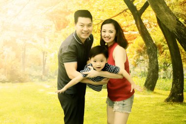 Mutlu küçük çocuk, sonbahar ağaçlarının arka planında parkta oynarken ailesinin yanında sallanıyor.