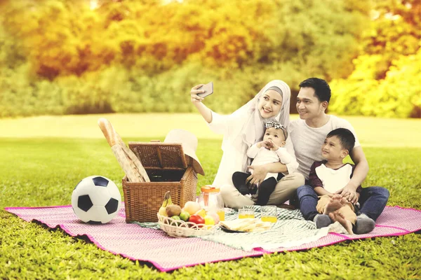 秋の木々を背景に公園を眺めながら 携帯電話で自撮り写真を撮るイスラム教徒の家族 — ストック写真
