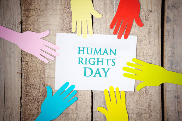 Top view of colorful paper hands with Human Rights Day text on the paper above wooden table